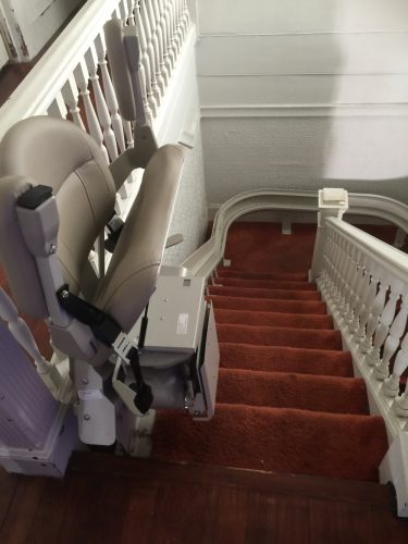 Stairlift parked at top step, seat folded.