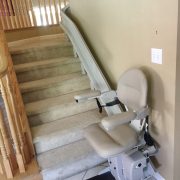 Stairlift parked at bottom landing, charging with seat down.