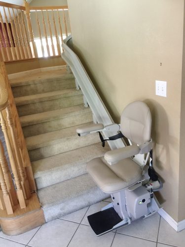Stairlift parked at bottom landing, charging with seat down.