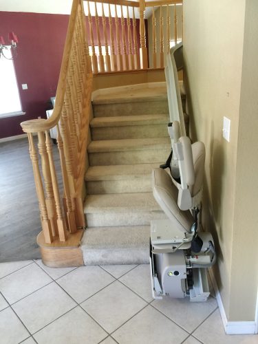 Stairlift parked at bottom landing, charging with seat up.